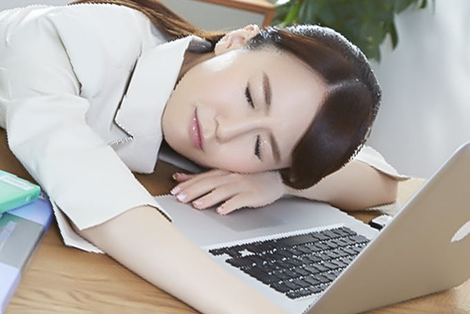 仕事中に疲れてパソコンの前で寝ている女性
