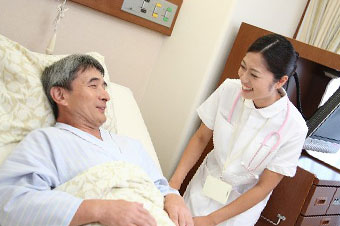 病院のベッドに寝て看護師と話をしている男性高齢者